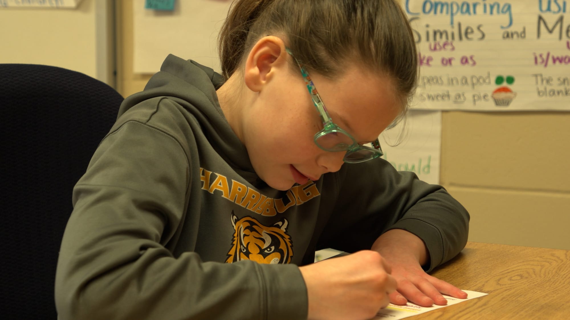 A student writes on a worksheet on her desk at school.