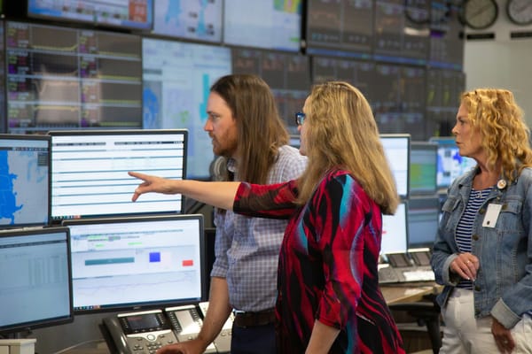 Two women and a man look at monitors in a room full of computers