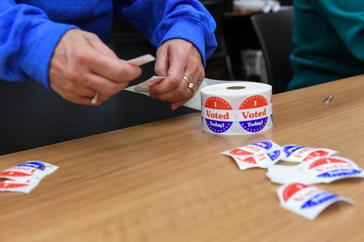 I Voted stickers are shown on a table as a poll worker takes one to hand out.