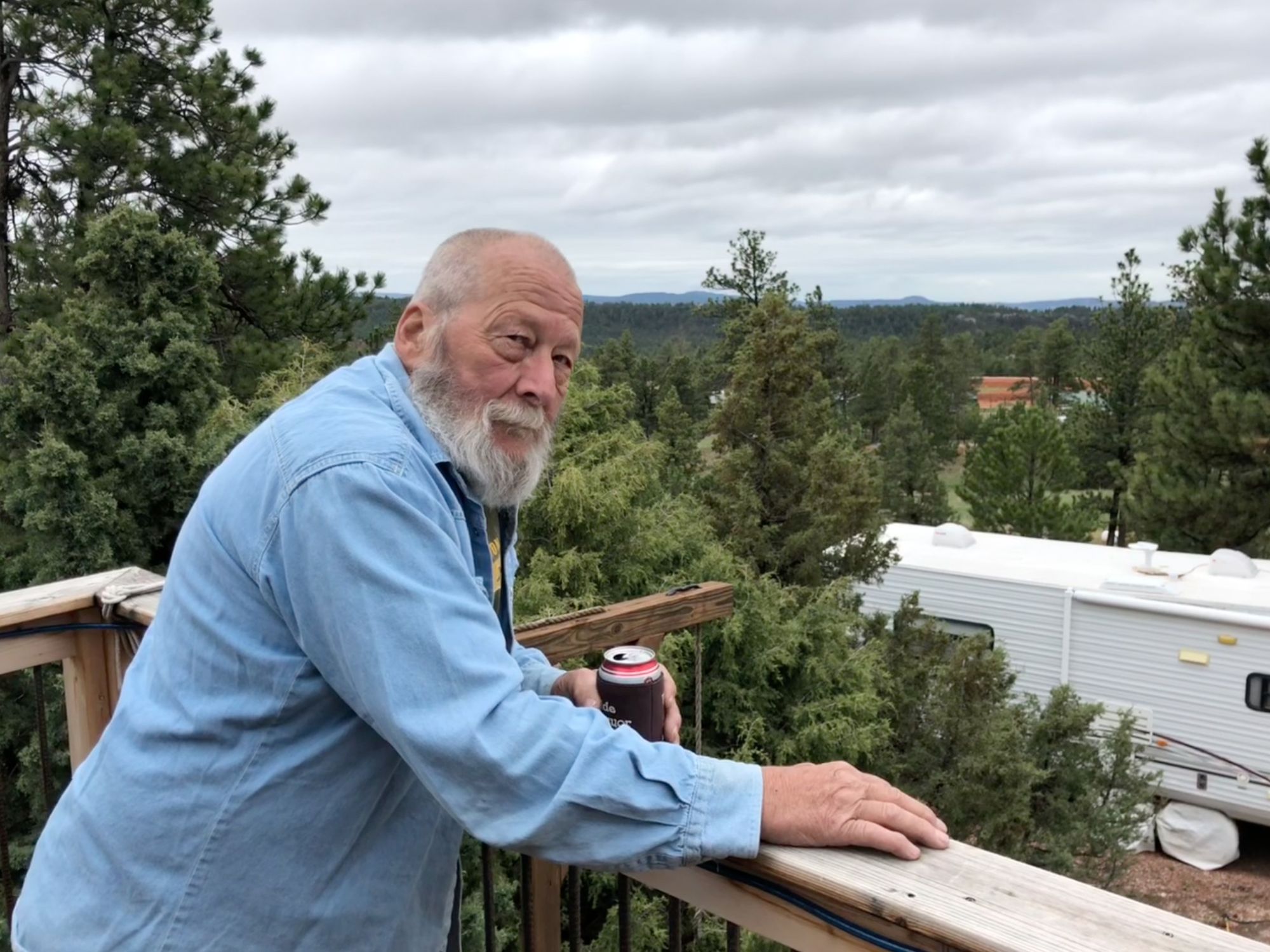 Karl Van Rump on porch overlooking compound in trees.