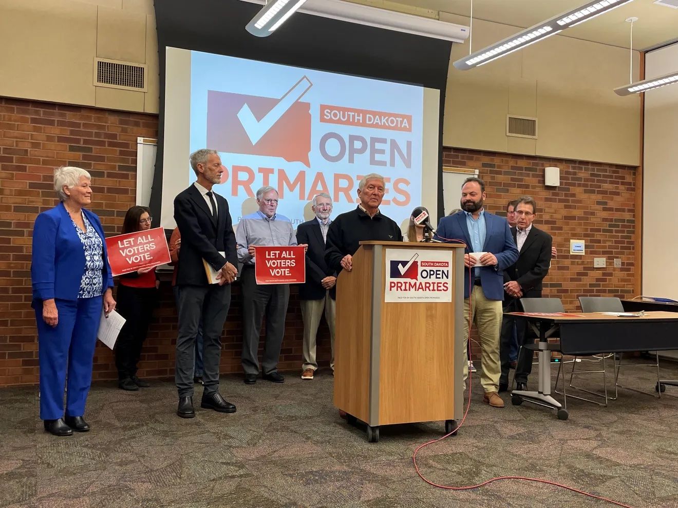 Members of the South Dakota Open Primaries groups stand behind a podium during a news conference